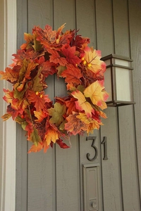 Detail of autumn maple leaf wreath with orange leaves and berries on a dark wooden door