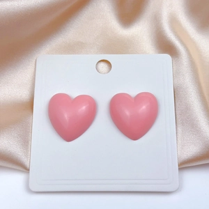 Macro shot of 3D pink heart-shaped stud earrings on satin background with display card