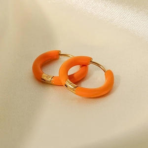 Primer plano de pendientes de aro esmaltados naranjas sobre fondo de seda beige