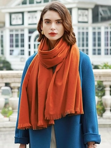 Detail of orange cashmere-like scarf with short fringes worn by a model in soft daylight