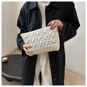 Detailed view of white quilted clutch bag with diamond lattice pattern held by model