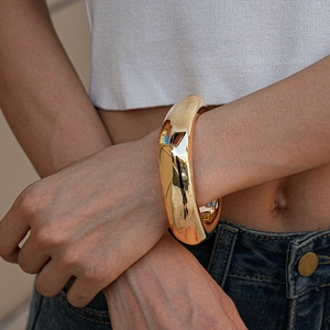 Close-up of a wide polished gold metal cuff bracelet on a model wrist with modern style