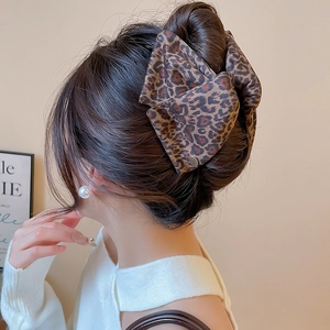 Macro shot of large leopard print fabric bow hair claw clip showing texture and design