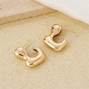 Detailed view of golden irregular liquid-style earrings on textured stone and fabric background