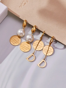 Détail macro de boucles d'oreilles dorées 18 carats avec perles et pompons lettre D