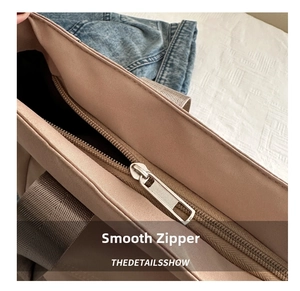 Detail view of smooth silver metal zipper and brown nylon handles on a large tote bag