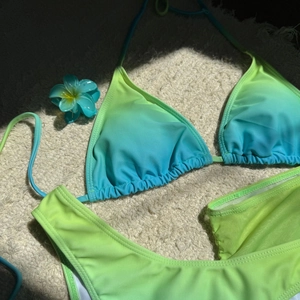 Détail à plat d'un bikini trois pièces en dégradé de couleurs avec une fleur de frangipanier