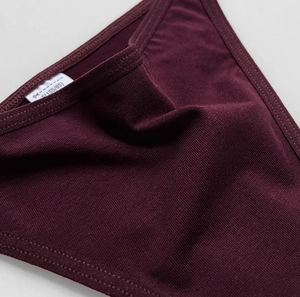 Macro shot of dark red ribbed knit cotton fabric showing texture and size S tag on thong