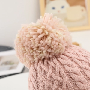 Detailed close-up of pink knit hat featuring soft pom-poms and intricate cable stitch texture