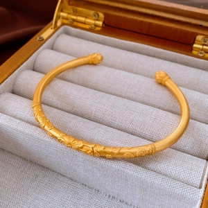 Close-up of vintage gold open bangle with intricate floral lotus carvings and matte finish