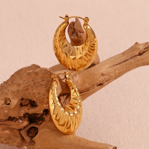 Detailed macro view of gold hollow oval hoop earrings with geometric pattern on wood