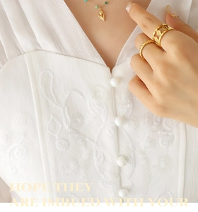 Detail of tulip pendant necklace and geometric gold rings on a model in white lace