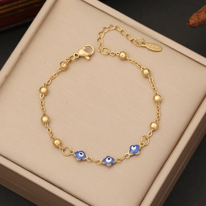 Macro detail of gold evil eye bracelet with blue enamel charms on a beige jewelry box