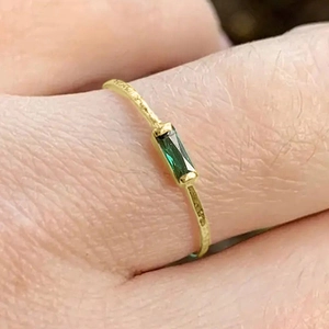 Macro detail of slim gold ring with a rectangular green gemstone on a finger