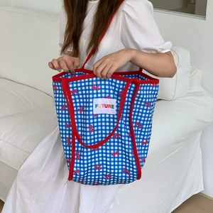 Detail of blue plaid canvas tote bag with red bow pattern and colorful FUTURE patch