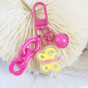 Close-up of pink metal keychain with a yellow acrylic butterfly on a white coral base
