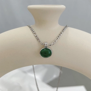 Detail of green aventurine pendant necklace with silver chain on a decorative ceramic vase