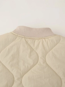 Detail of ribbed knit collar and diamond quilted stitching on beige jacket