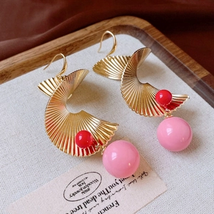 Details von goldenen Spiralohrringen mit pinken Perlen auf einem Holzständer