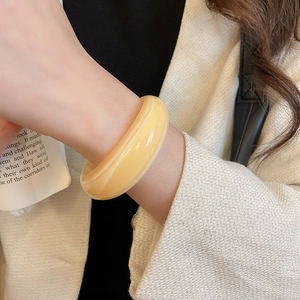Gros plan d'un large bracelet en résine jaune crème marbrée sur le poignet d'un mannequin