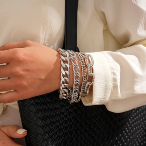 Close-up of stacked silver metal chain bracelets with various link styles on model wrist