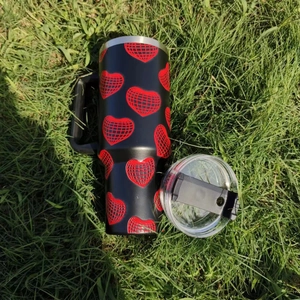 Top view of a 40oz black tumbler with red heart patterns on green grass background