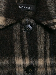 Détail du col d'une veste en laine à carreaux marron et gris avec un bouton noir mat