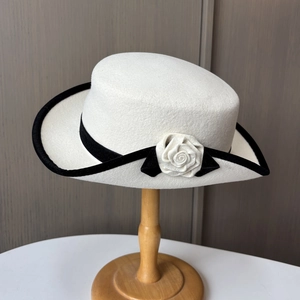 Gros plan sur un chapeau en feutre de laine blanc avec bordure noire et détail de camélia