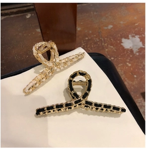 Detail of woven chain hair clips in black and white styles on minimalist surface