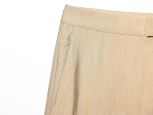 Detail van champagne goud satijnen broek met fijne stiksels en geplooide tailleband