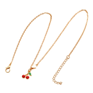 Dettaglio collana dorata con ciondolo ciliegia rossa, cuore, chiusura e estensione
