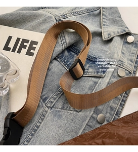 Detail of adjustable brown woven shoulder strap with black plastic buckle on denim background