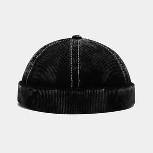 Detail of black corduroy brimless cap featuring beige contrast stitching and top button