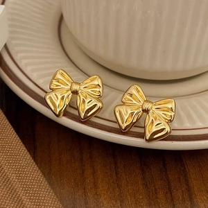 Close-up of polished gold bow stud earrings placed on a white ceramic saucer