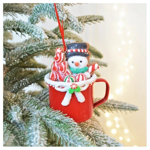 Festive red cup ornament with a snowman and candy cane on a snowy Christmas tree branch