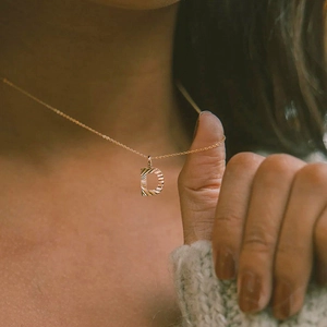 Macro detail of golden letter D pendant with pleated texture on a fine link chain