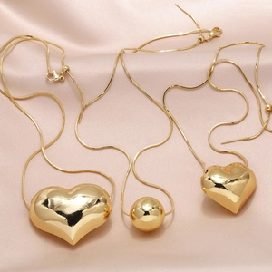 Polished gold heart pendant necklace with snake chain on soft pink satin background
