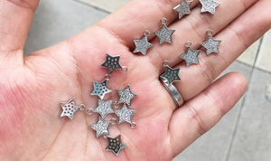 Handheld view of mini star-shaped silver pendants with sparkling zircon pave setting