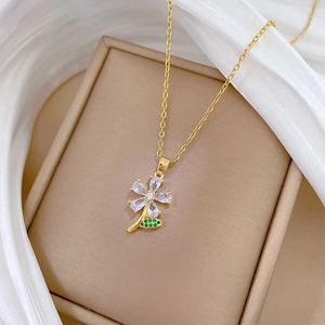 Detail of flower necklace with green leaves and clear zircon on a beige jewelry box
