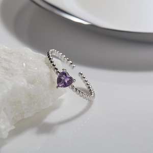Macro shot of silver rope band ring with heart-shaped purple gemstone on white crystal