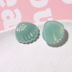 Dettaglio di due ciondoli a conchiglia in resina verde con glitter dorati su vassoio