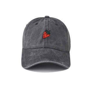 Detailed view of strawberry embroidery and washed denim texture on a dark grey baseball cap