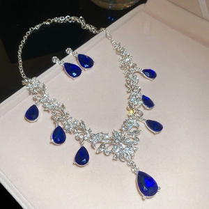 Close-up of elegant silver necklace and earring set with blue teardrop crystals in a gift box