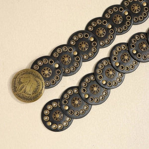 Detail of black round leather discs with vintage copper floral studs and large round buckle