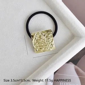 Macro detail of 3.5cm gold square hair tie with irregular fluid texture on black elastic