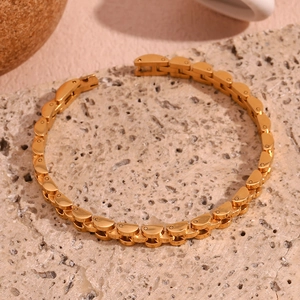 Macro detail of 18K gold-plated stainless steel link bracelet on a beige stone base