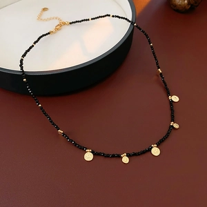 Détail d'un collier de perles noires avec des pendentifs dorés ronds texturés