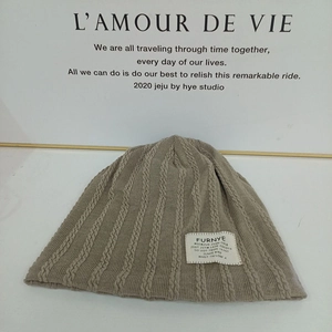 Detail of khaki cable knit beanie texture with a minimalist white fabric brand patch