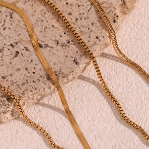 Close-up of golden snake and box chains on natural stone showing fine metal texture