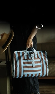 Close-up of a striped travel organizer bag with handle and front pocket in use